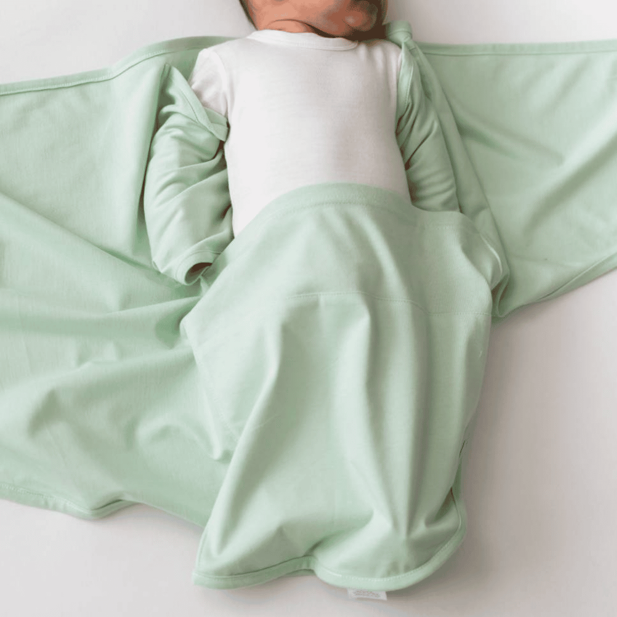 Newborn baby wrapped in a light green swaddle on a white background