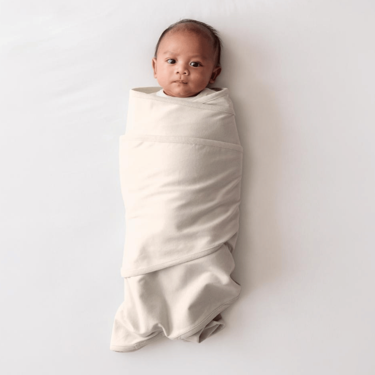 Baby wrapped in a beige swaddle on a light gray background