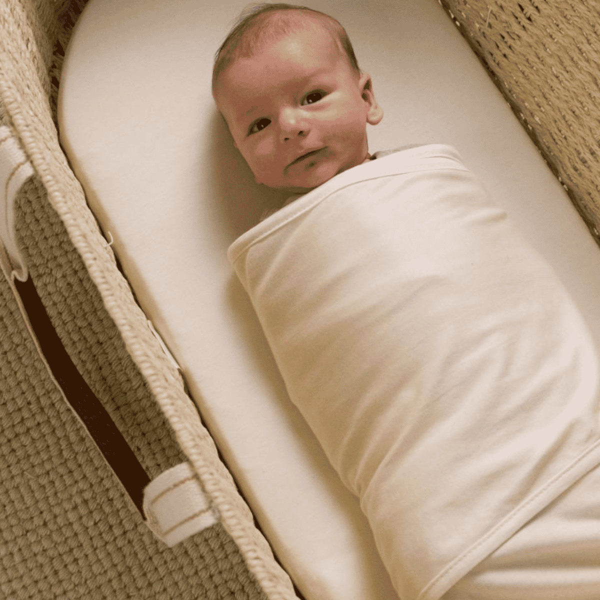 Newborn baby wrapped in a white blanket lying in a crib.