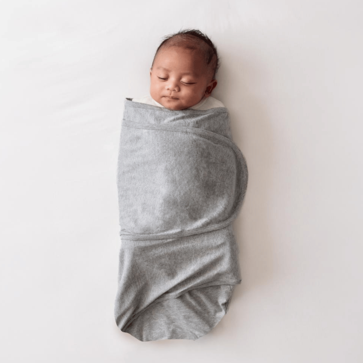 Newborn baby swaddled in a gray blanket on a white background