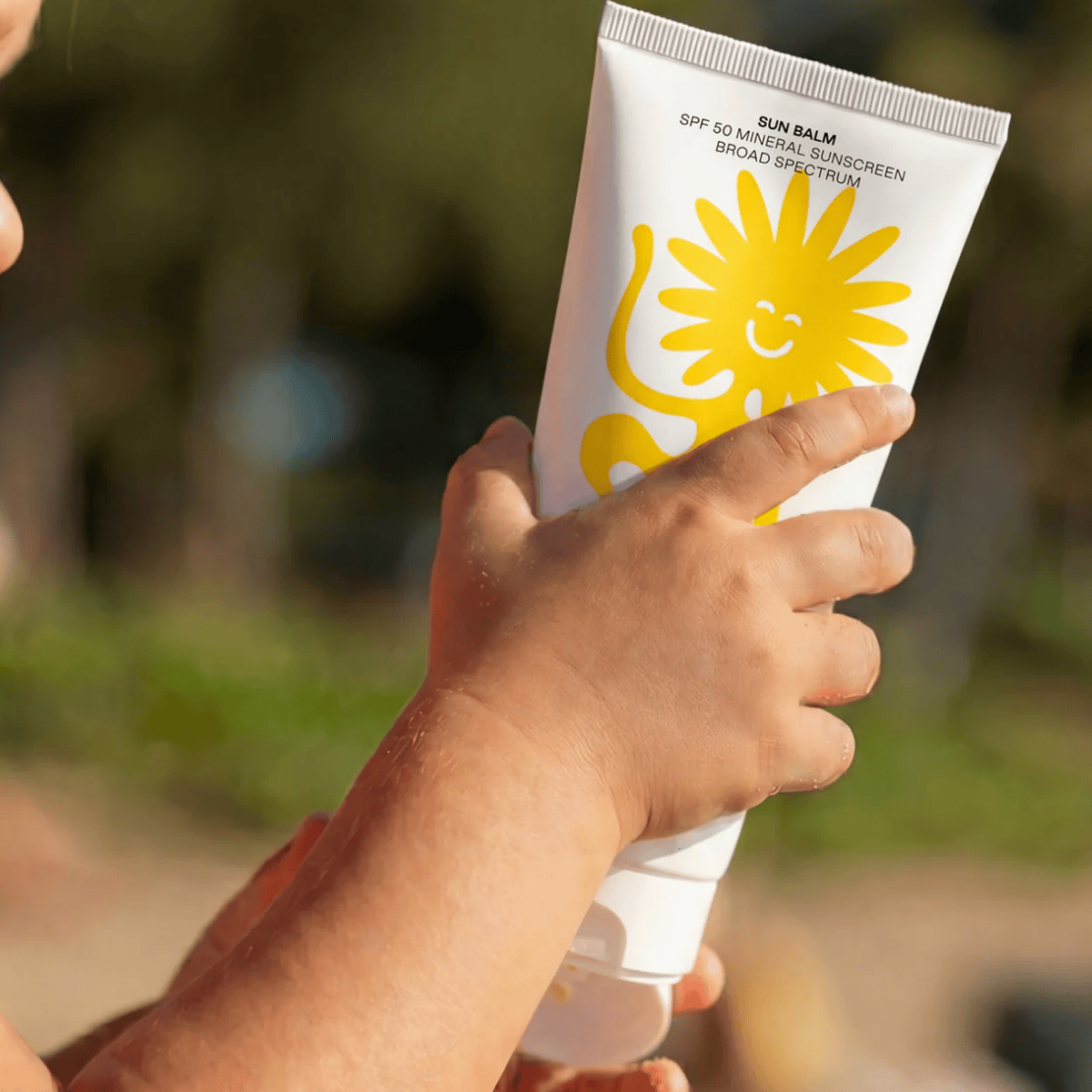 Hand holding a tube of sunscreen with a sun design on a blurred natural background