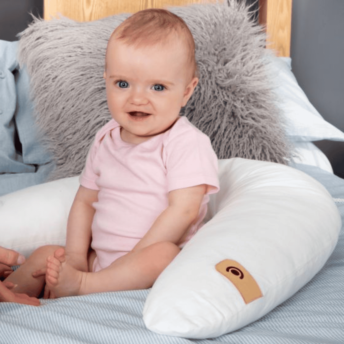 Baby in a pink outfit sitting on a white cushion with a gray pillow in the background