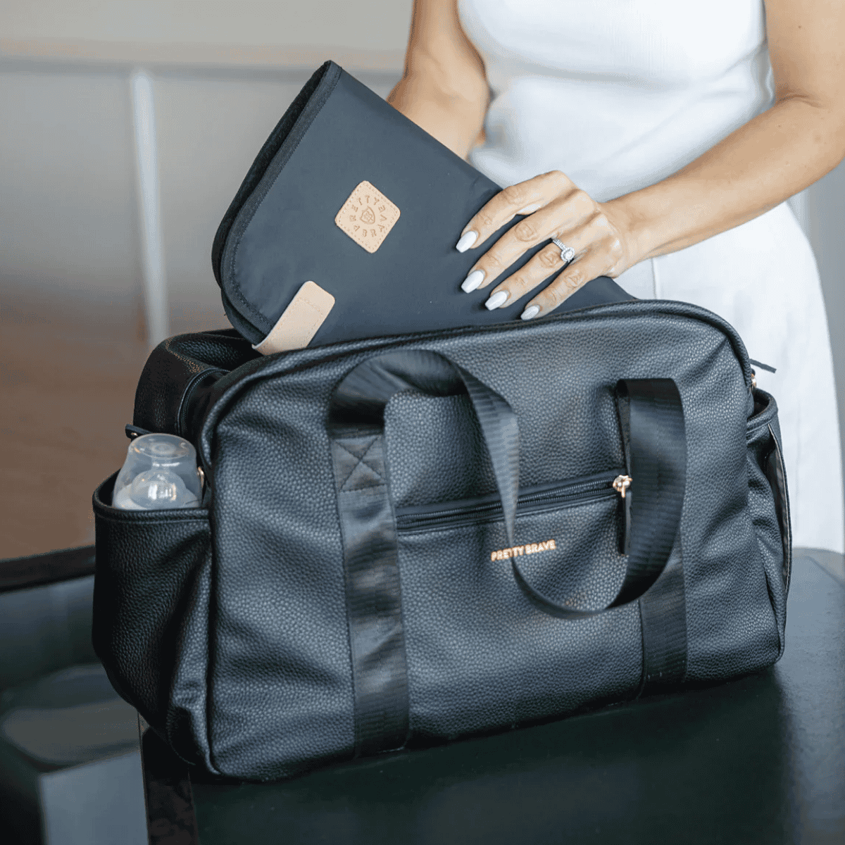 Person holding a black duffel bag with a visible brand logo, sitting on a chair.