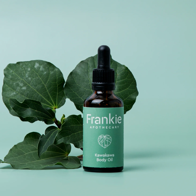Bottle of Frankie Apothecary Kawakawa Body Oil with green leaves on a light blue background