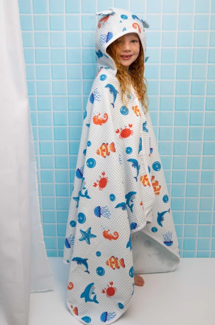 Child wrapped in a colorful towel with sea creature patterns against a blue tiled wall.