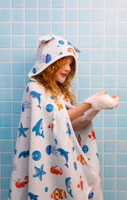 Child wrapped in a hooded towel with animal patterns against a blue tiled wall.