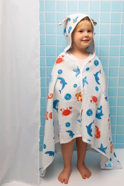 Child wrapped in a colorful hooded towel with sea creature patterns in a bathroom.