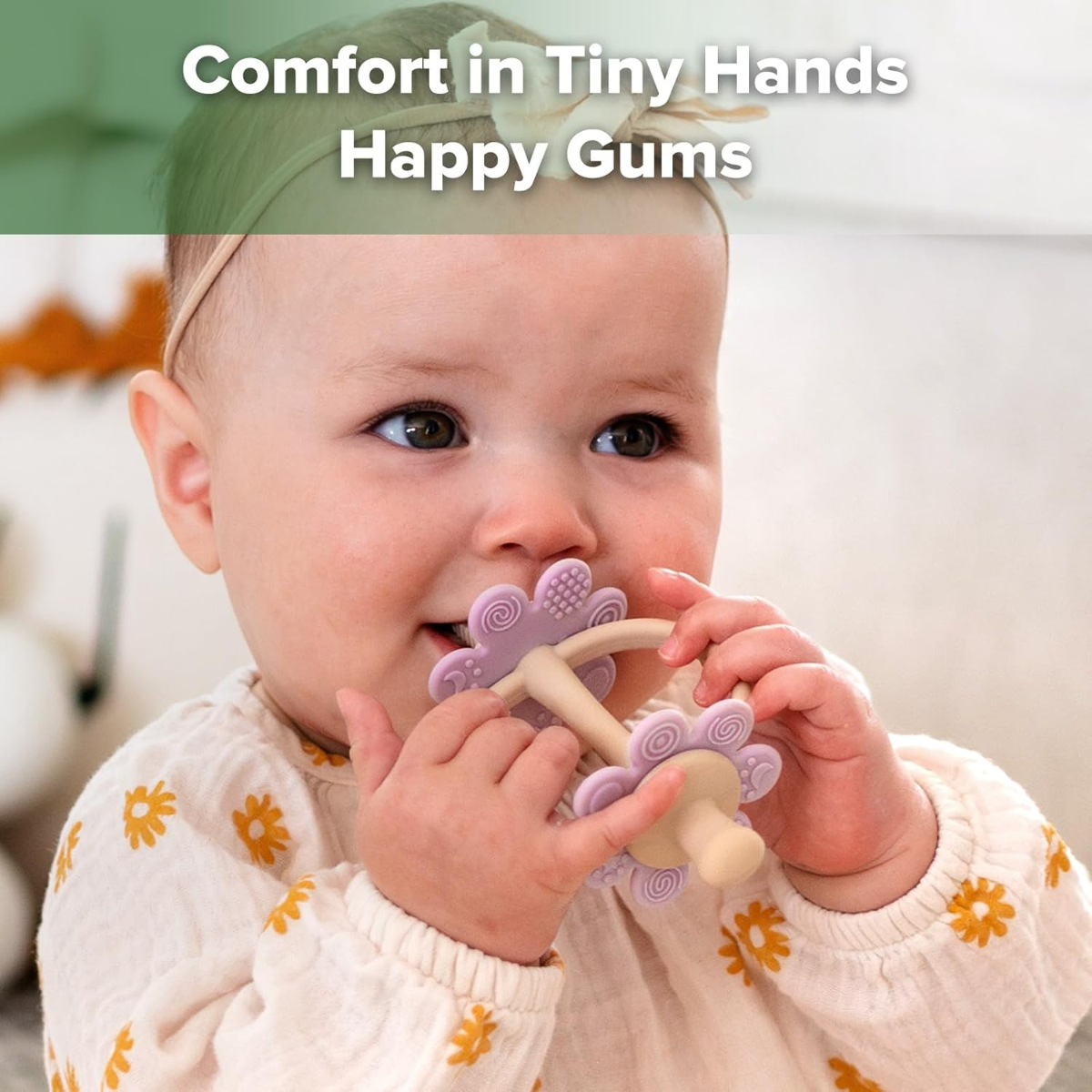 Baby holding a purple and white teething toy with text 'Comfort in Tiny Hands Happy Gums' above.