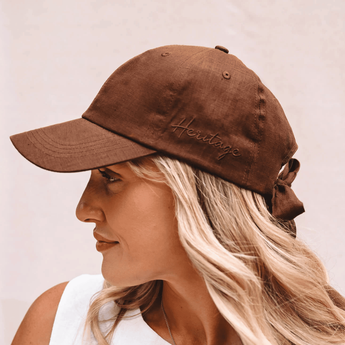 Woman wearing a brown cap with 'Heritage' embroidery on a beige background