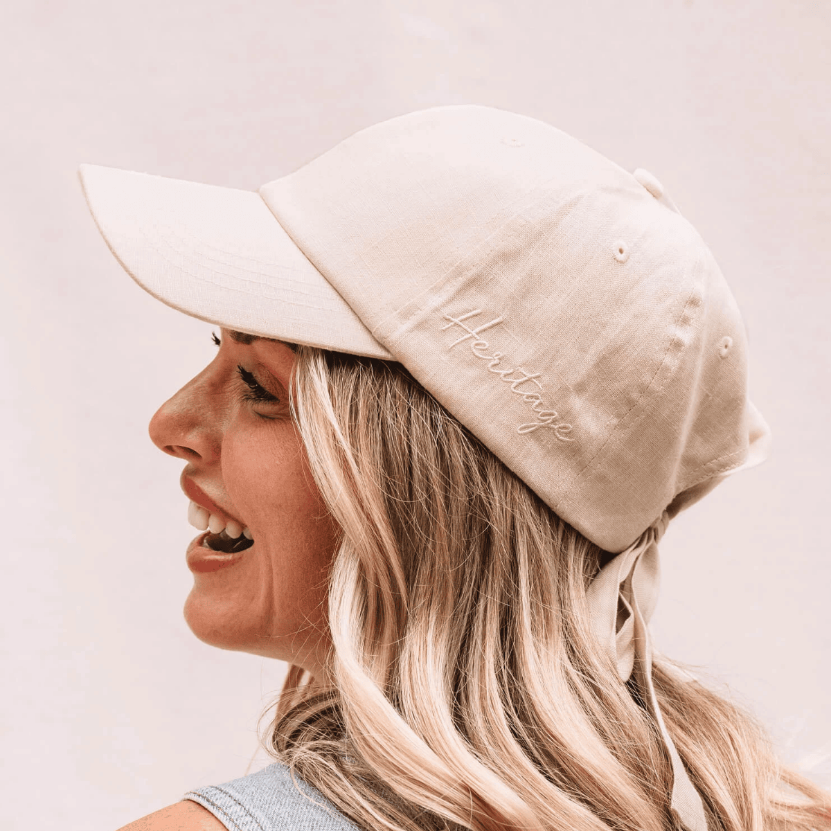 Woman wearing a beige cap with 'Heritage' embroidery on a light background