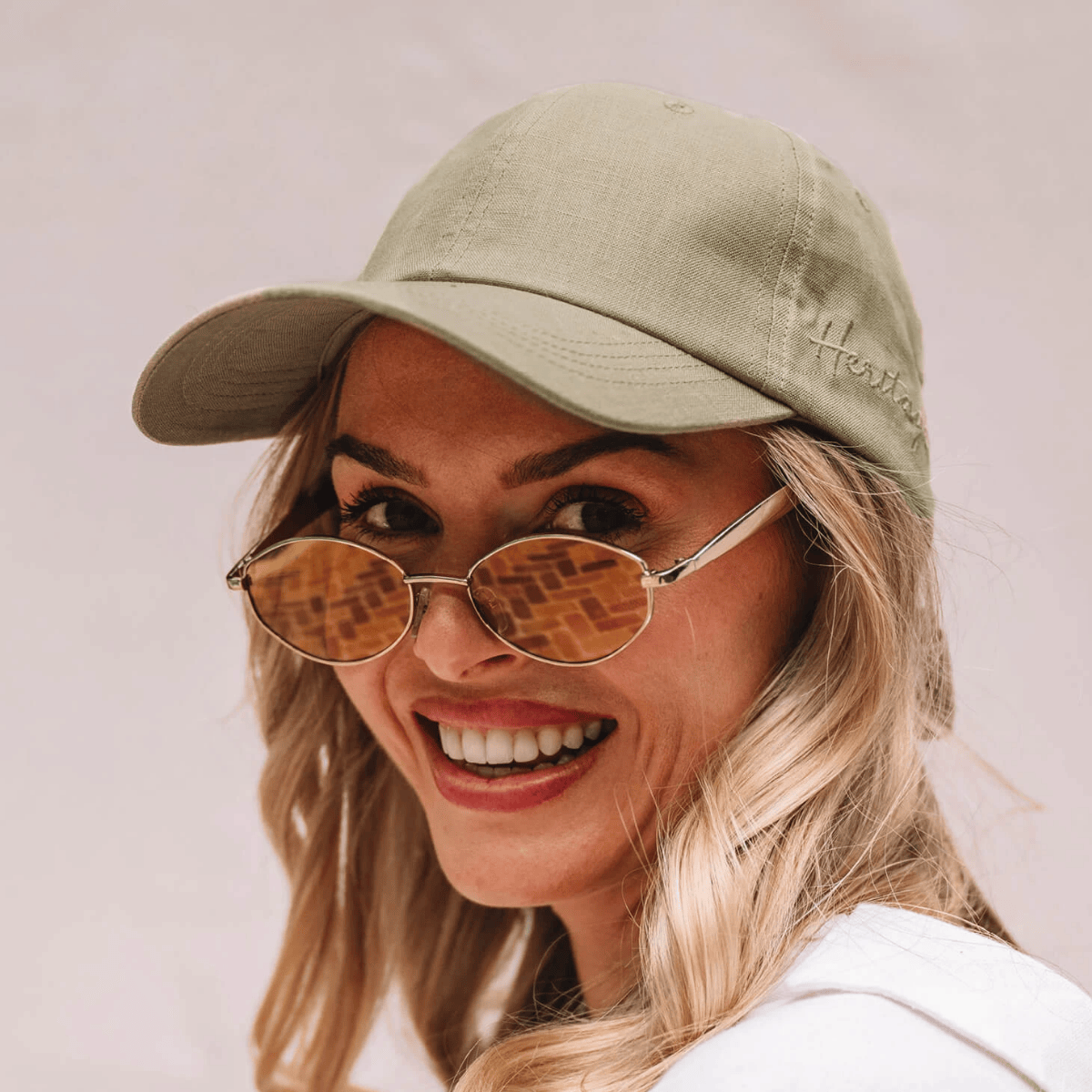 Woman wearing a light green cap and sunglasses with a plain background
