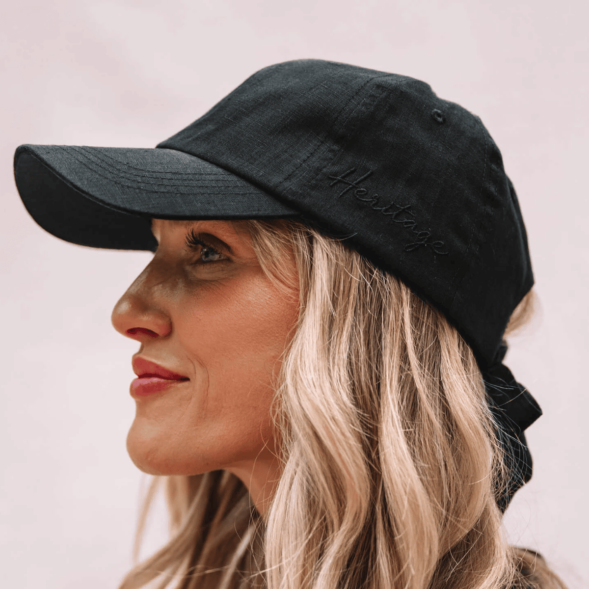 Woman wearing a black cap with 'Heritage' logo on a plain background