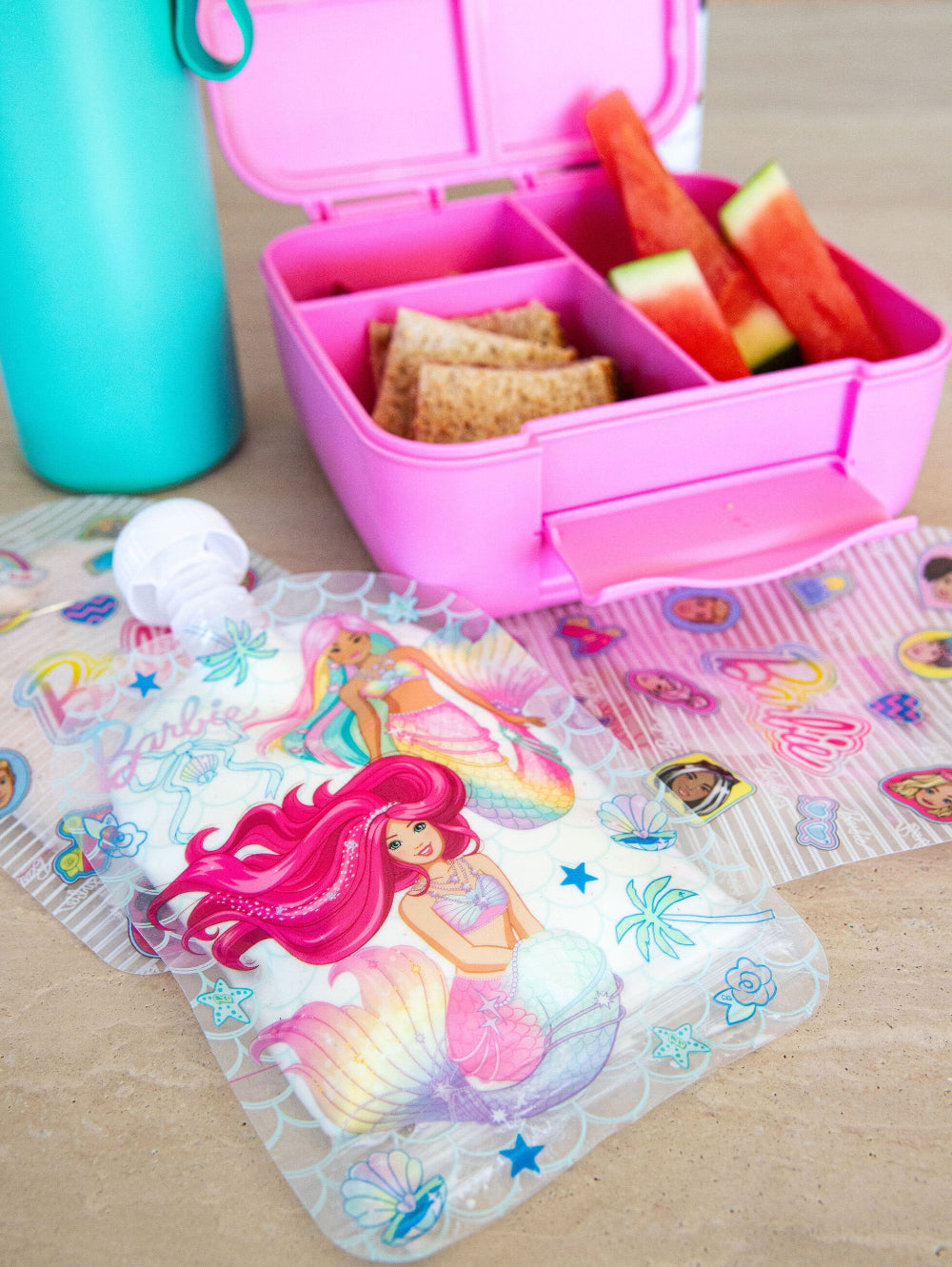 Pink bento box with snacks and a mermaid-themed ice pack on a table.