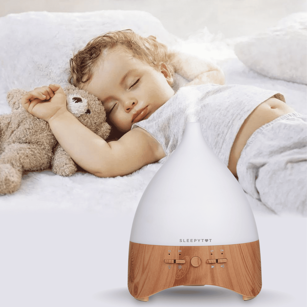 Child sleeping with a teddy bear next to a SLEEPYTIME diffuser on a white bed.