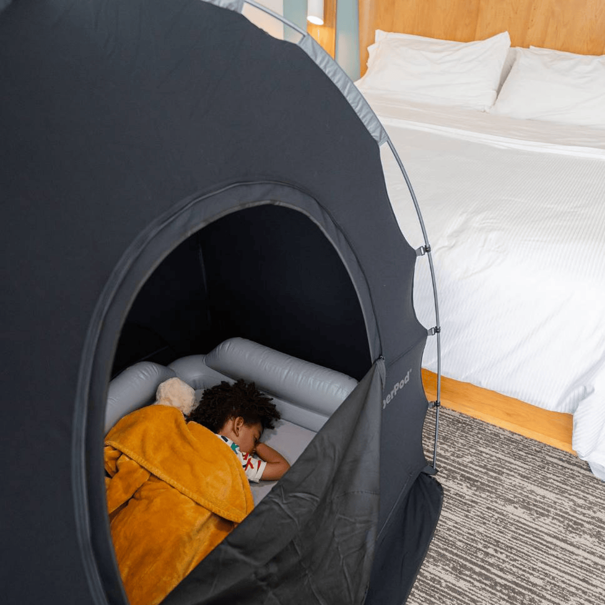 Child lying inside a portable SlumberPod play tent in a bedroom.
