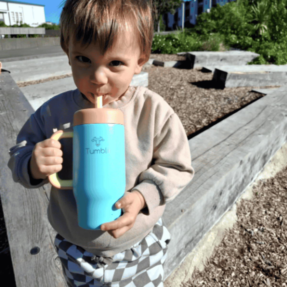 Child holding a blue tumbler with a straw outdoors