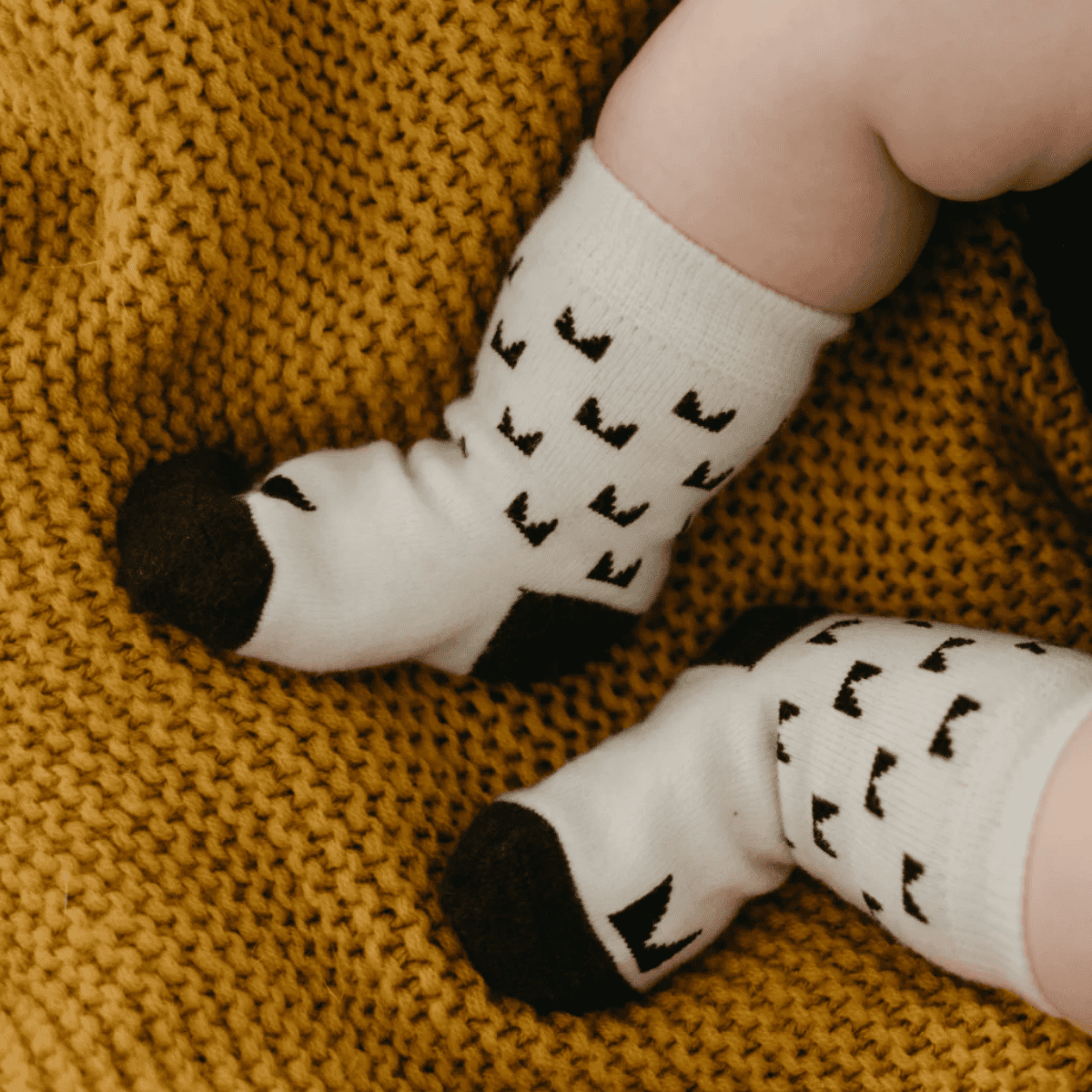 Baby's feet wearing white socks with black patterns on a yellow textured blanket