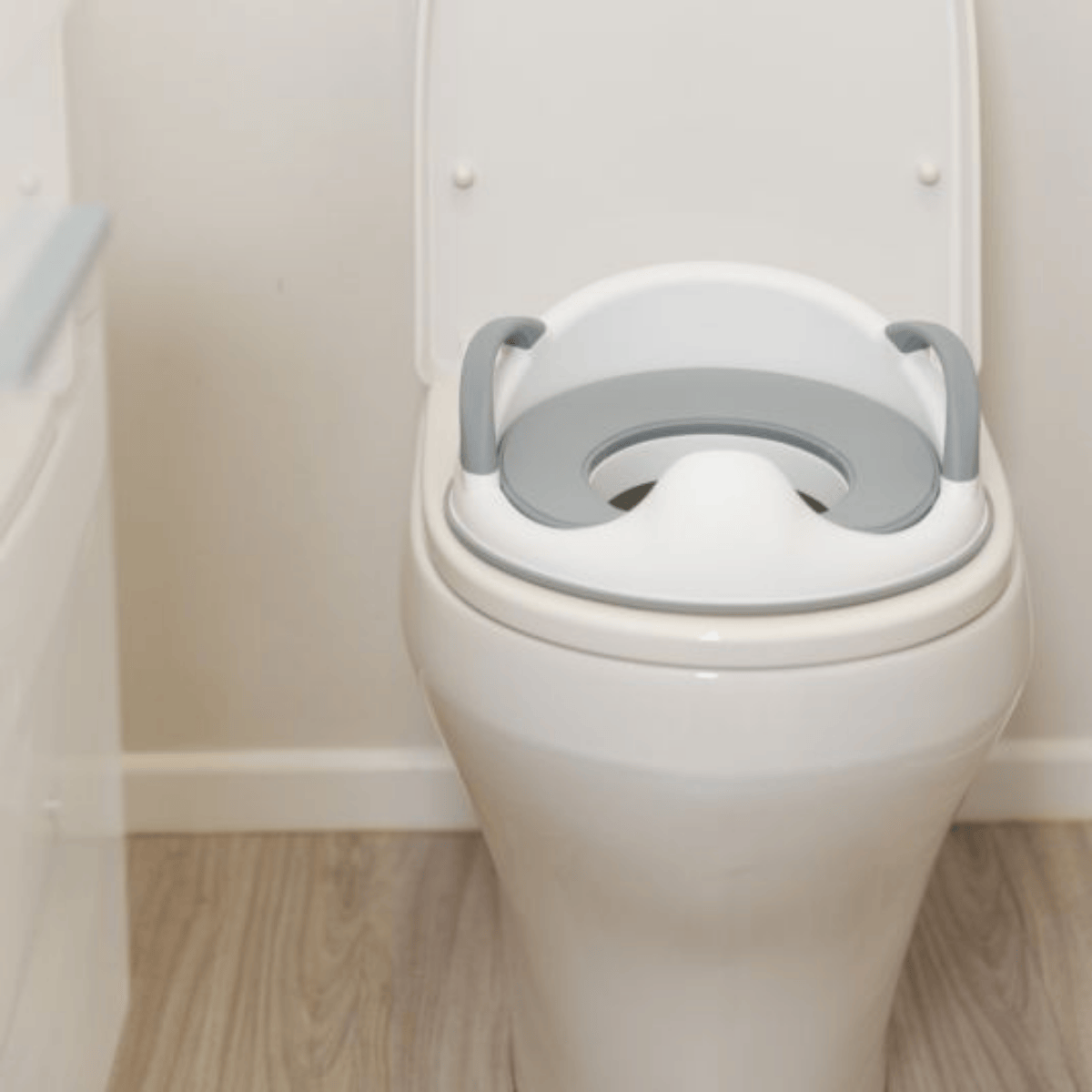 White toilet with a gray raised seat in a bathroom setting