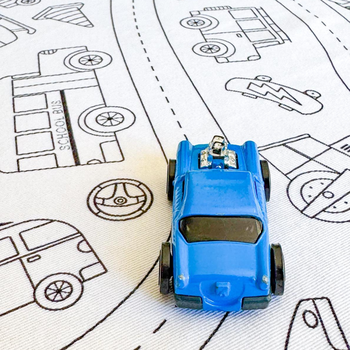 Blue toy car on wheels in motion colouring in table cloth a road drawing with various vehicle outlines.