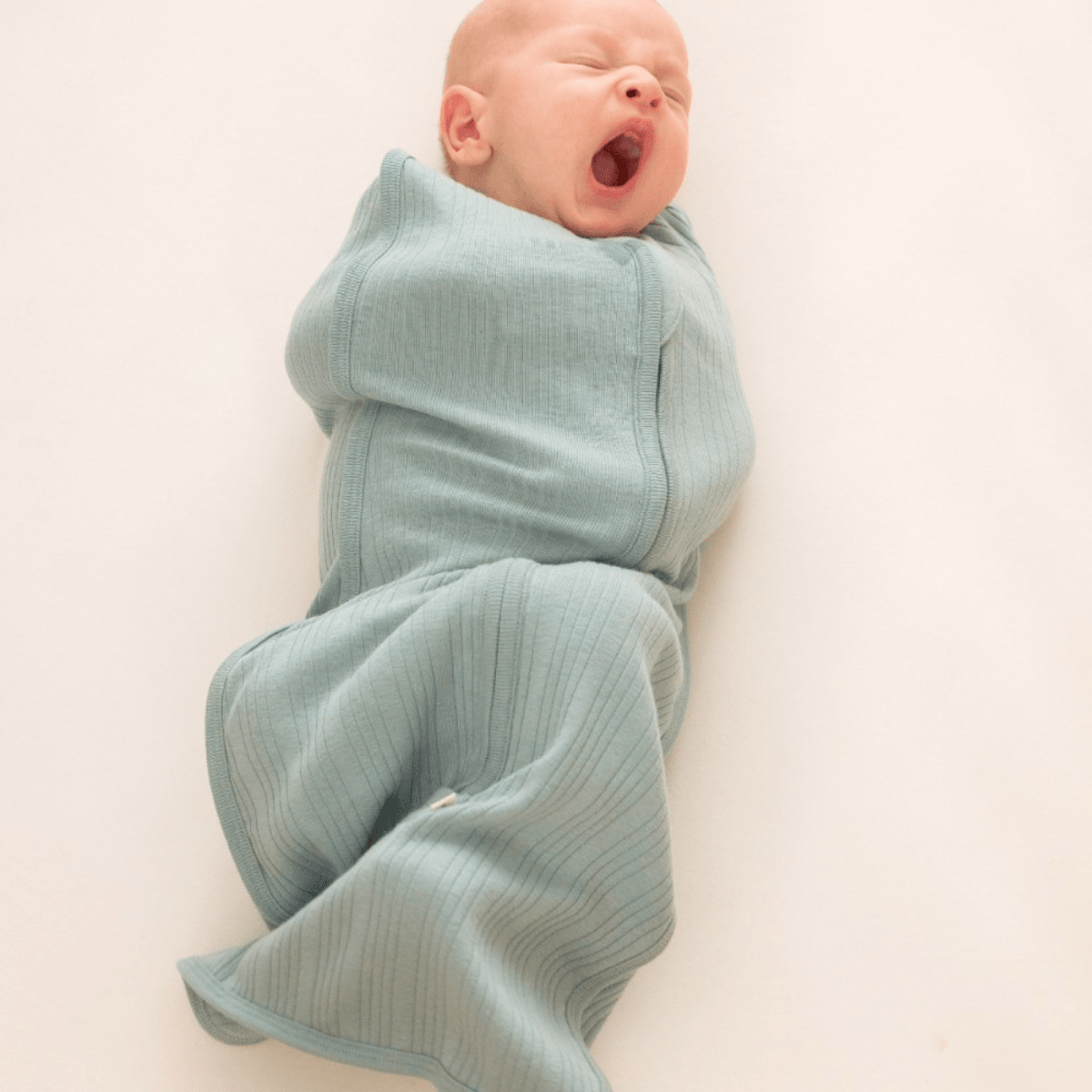 Newborn baby wrapped in a light blue swaddle on a white background