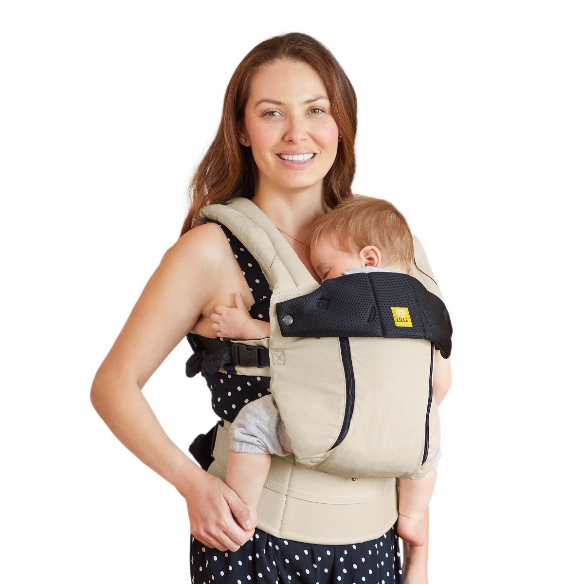 Woman holding a baby in a beige and black baby carrier against a white background