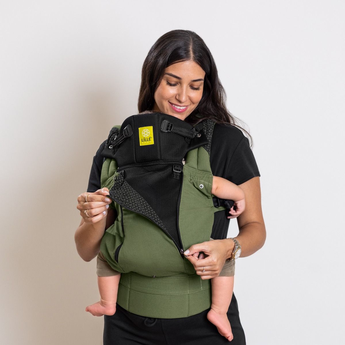 Woman using a olive green and black baby carrier against a plain background