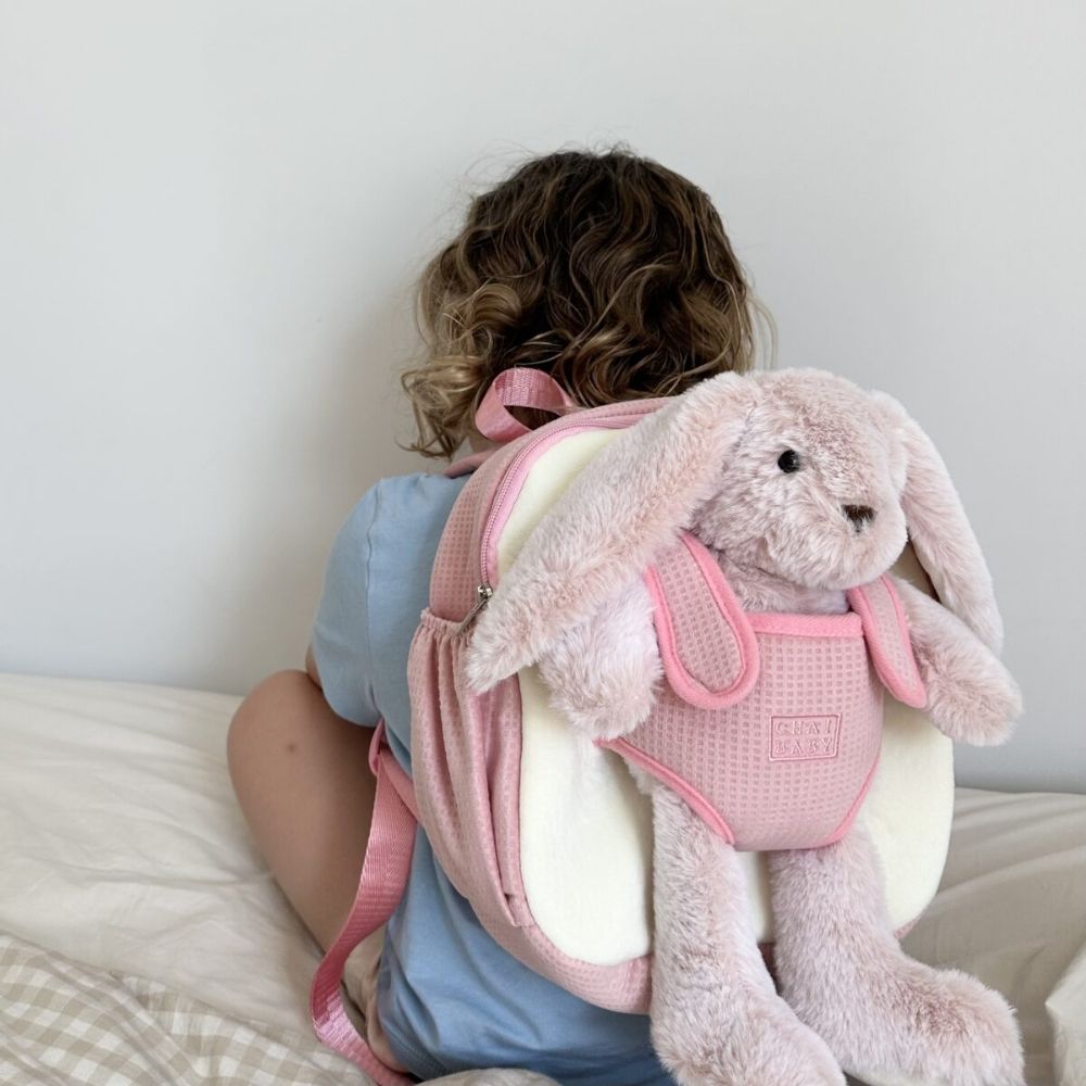 A child wearing the pink bunny Chai baby backapck showing her teddy in the carrier it comes with.