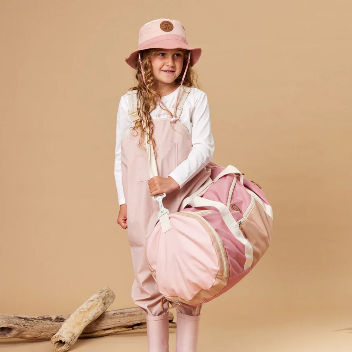 Young girl in pink outfit with matching bag against a beige background