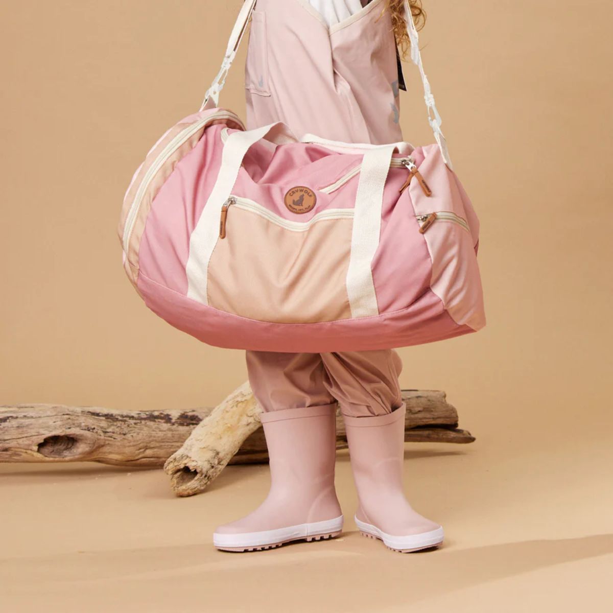 Pink duffel bag with beige accents on a white background with a girl in background showing how the bag can be drapped on shoulder