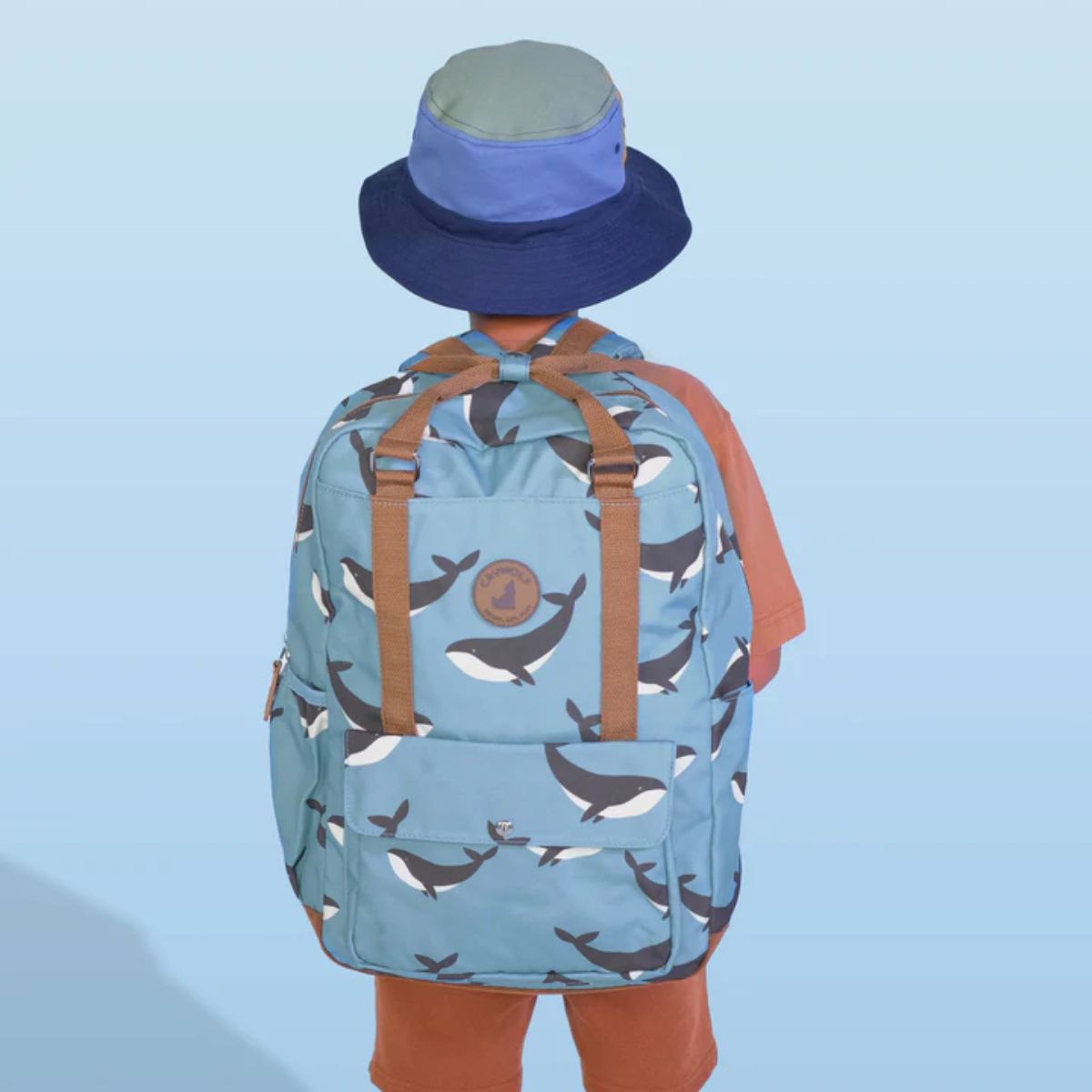 Person wearing a blue backpack with whale pattern and a matching hat on a light blue background