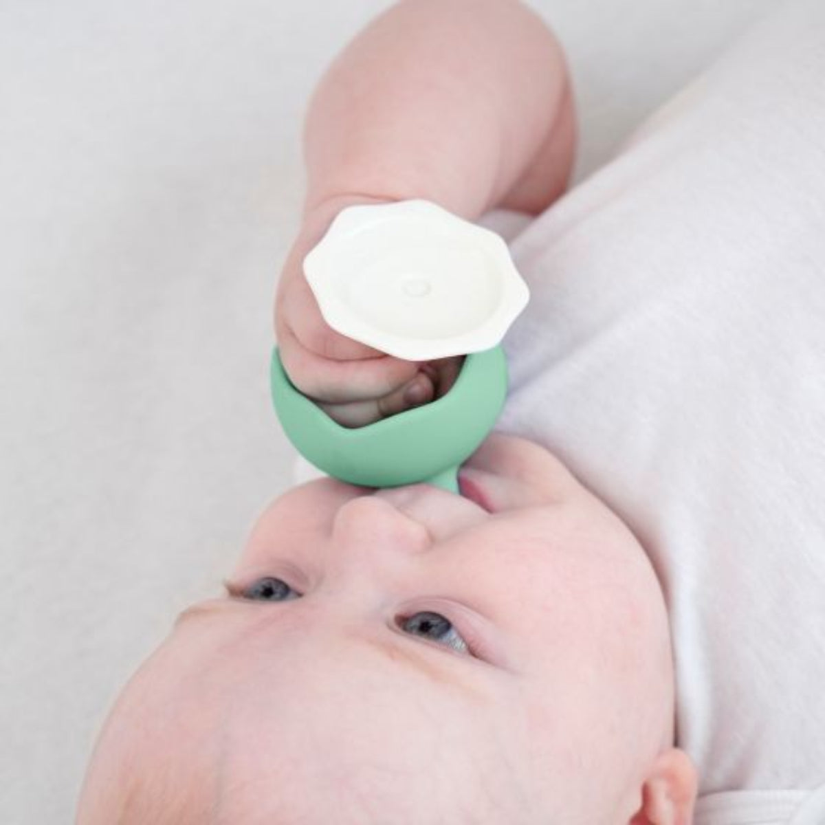 Baby holding a green teething ring with a white teether.