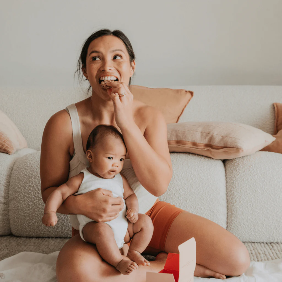 Woman sitting on a couch with a baby, both looking up and smiling.