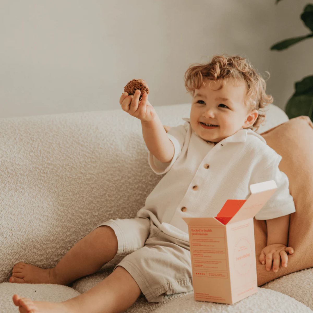 Child sitting on a couch holding a cookie with a box next to them.