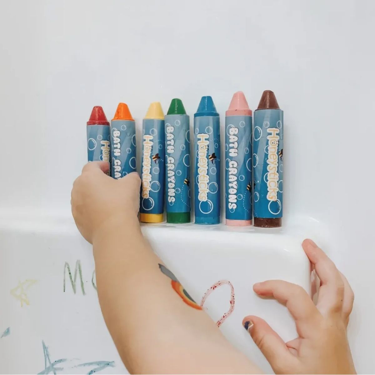 A girl drawing with the bath crayons inside the bath.