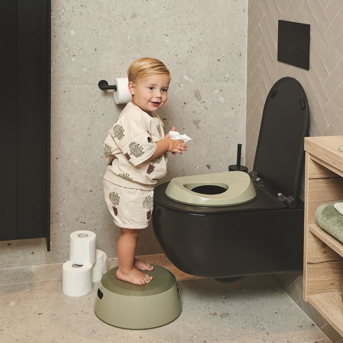 Child using a black toilet with a step stool in a bathroom setting
