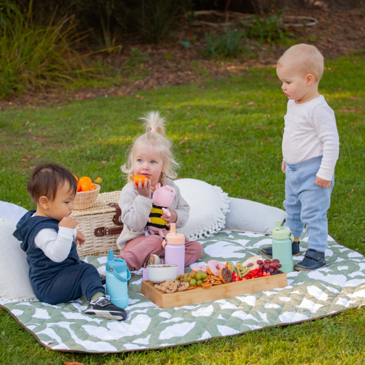 Three children having a picnic on a blanket in a park