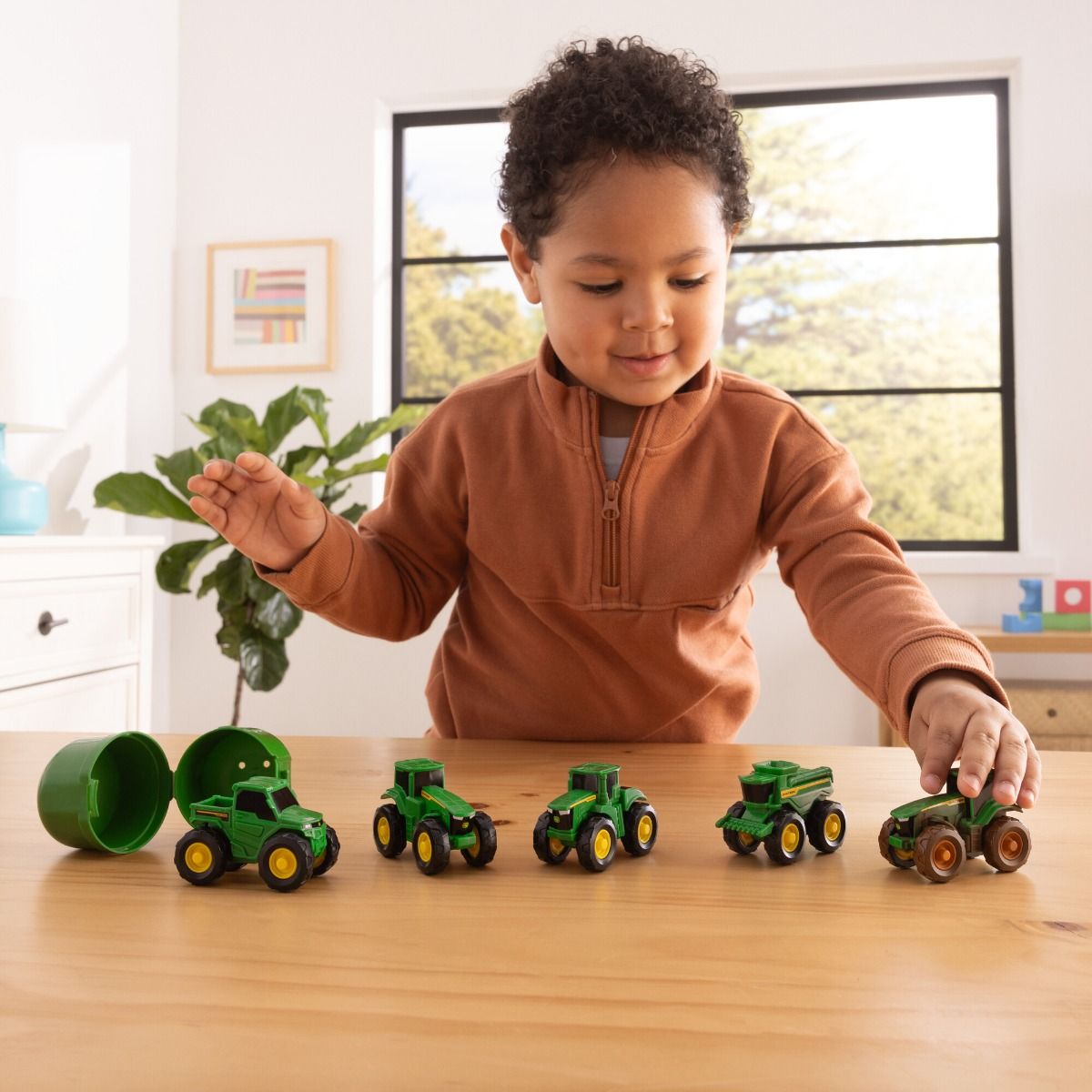 Child playing with John Deere  toy tractors on a wooden table