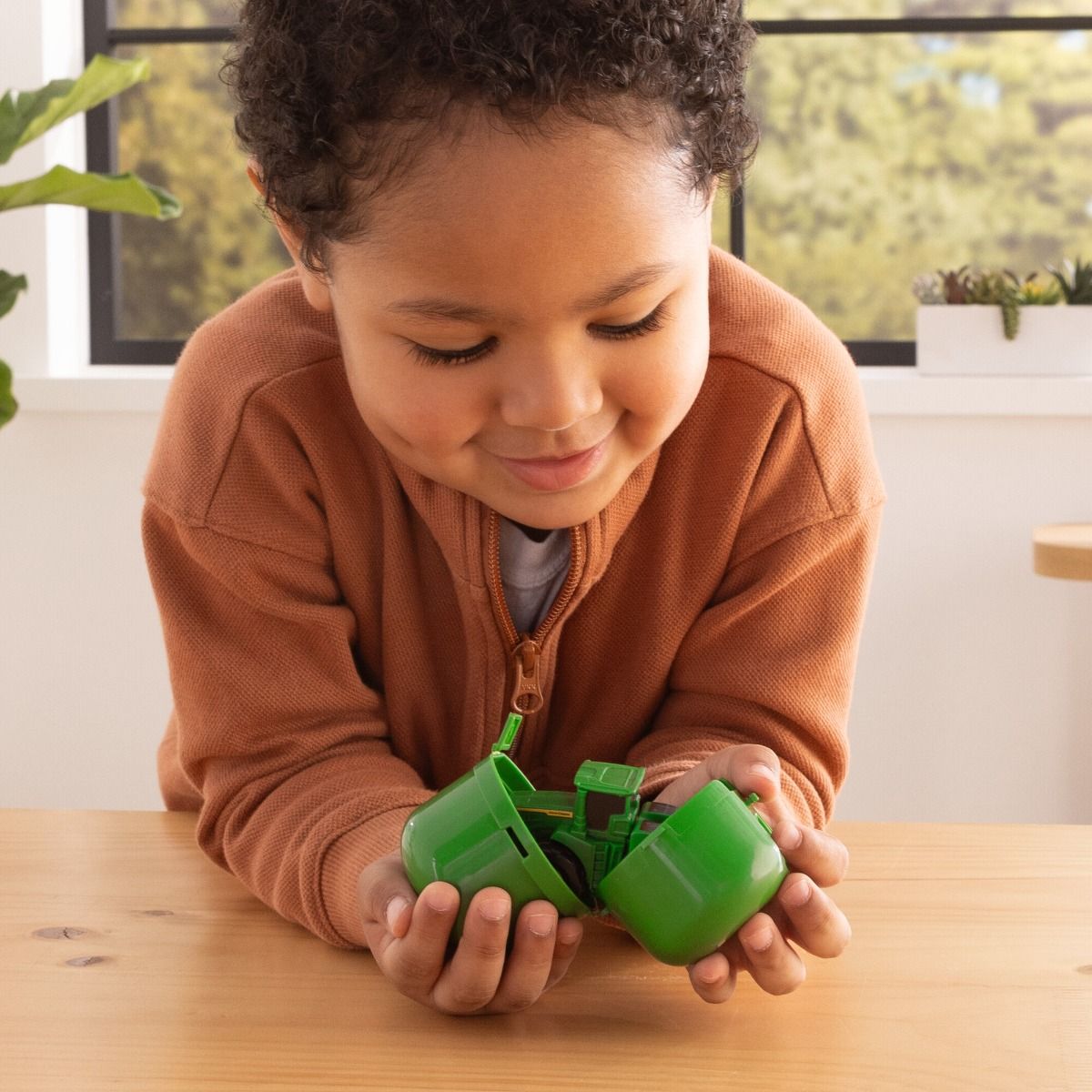 Child playing with a green John Deere  toy car indoors