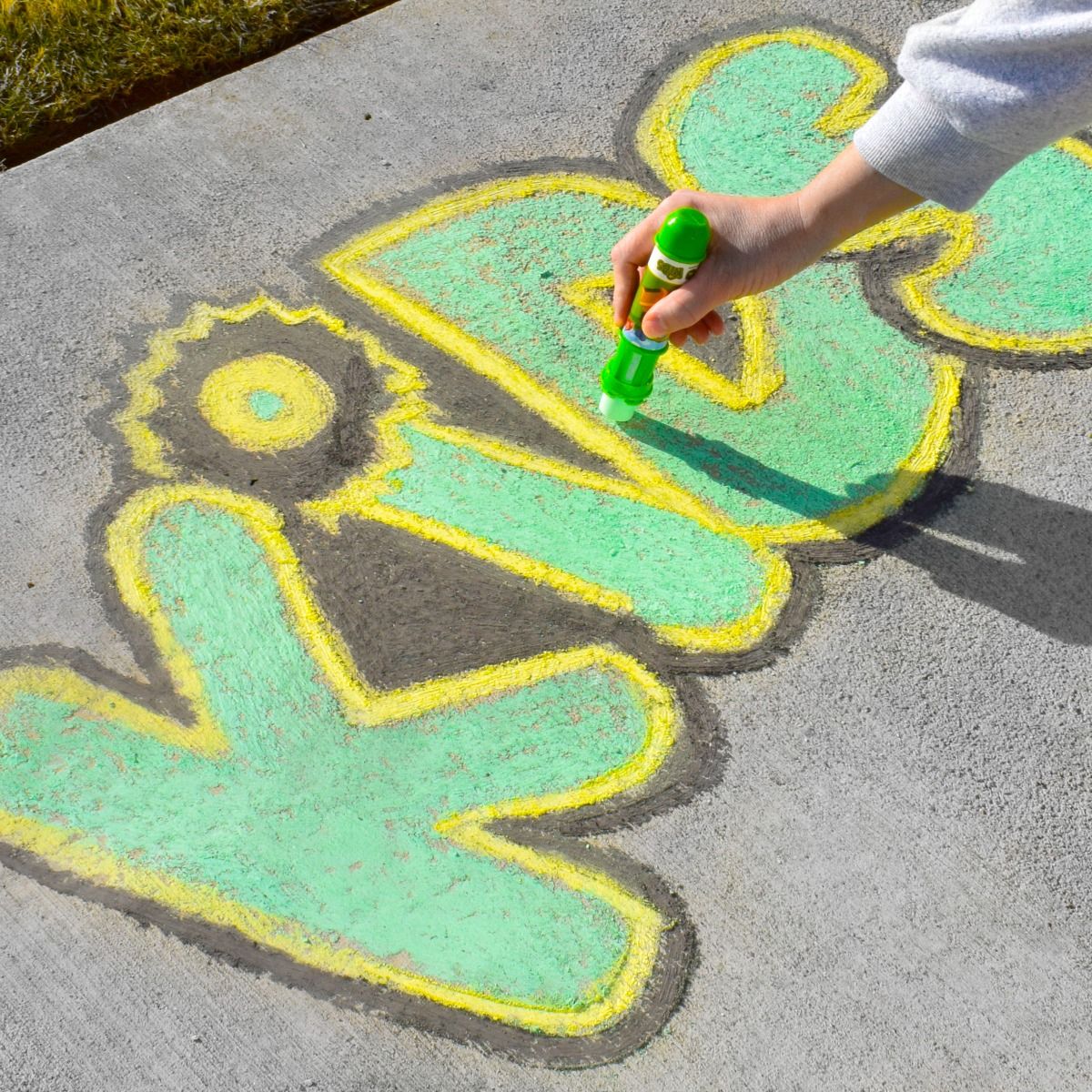 Person drawing a picture with green chalk on a concrete surface