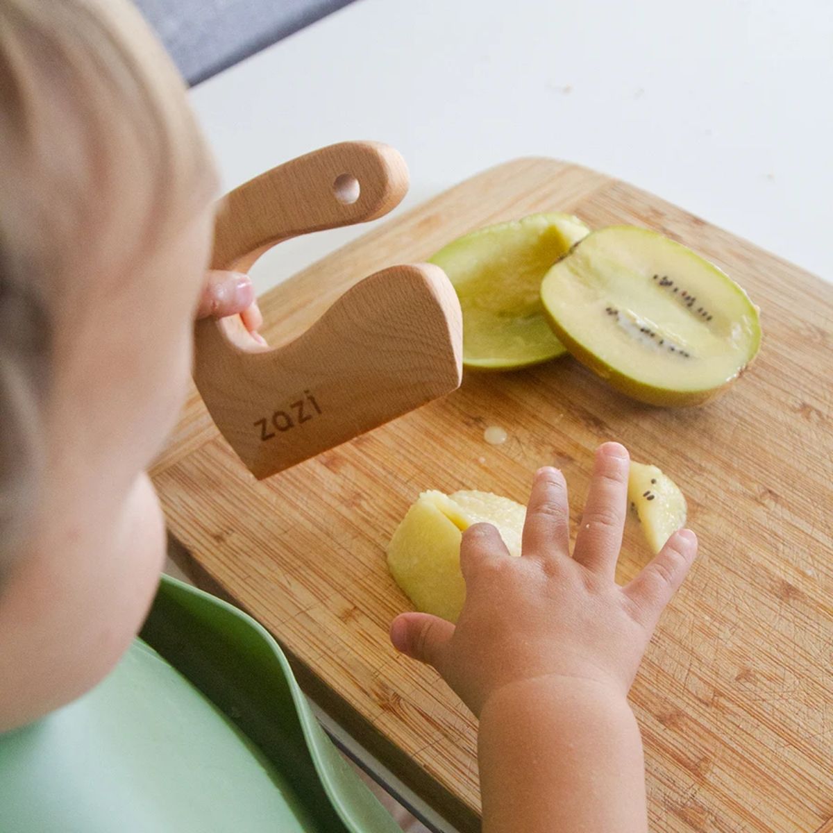 Child using a wooden safety knife on a cutting board with sliced apples